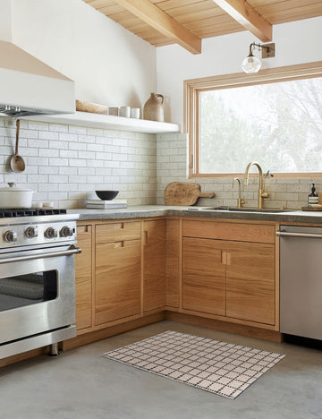 #size::1-9--x-2-10- #size::2--x-5- | The Sebou natural and black dotted machine washable mat lays in a kitchen with a subway tile backsplash and wooden cabinetry