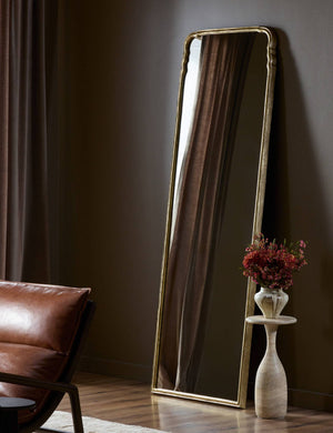 Coudray serpentine gold leaf frame floor mirror leaning against a wall