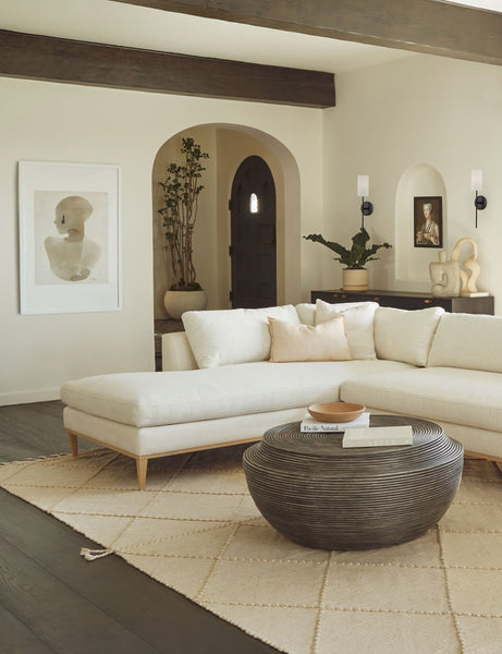 #color::white #size::32.25--x-47.25- #size::38.25--x-56.25- | The Sara singh back drop portrait neutral toned wall art by Stampa is hung in a living room with a white linen sectional sofa, a round wooden coffee table, and a textured beige rug