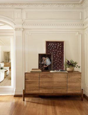 The Crane stencil 2 magenta and white wall art by ZBC house sits atop a wooden sideboard with a portrait painting and a stack of books