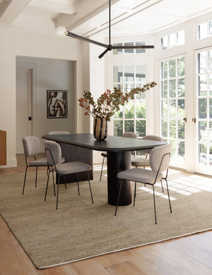 The Heritage wheat rug lays in a dining room with wrap-around windows, a black dining table, and upholstered dining chairs