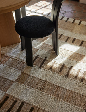 Tempo Flatweave Jute Rug by Elan Byrd under a black dining chair.
