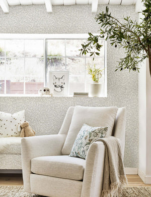 The Dainty Leaves floral Wallpaper by Rylee + Cru is in a nursery with a natural linen swivel chair and a woven brown rug