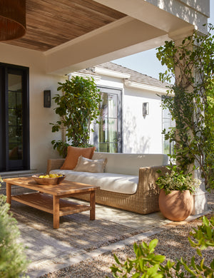 Gally teak and wicker outdoor coffee table and wicker sofa in a covered outdoor space.