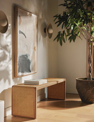 Canistel woven cane waterfall bench by Carly Cushnie styled with a large abstract canvas art piece and two disc wall sconces.