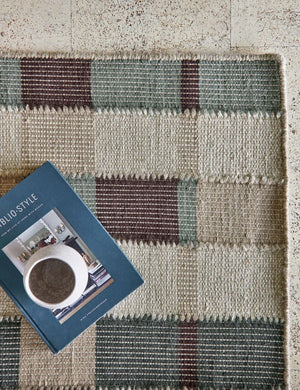 The corner of the Marli Rug under a ceramic mug and a blue book