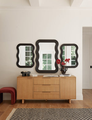 The Hillard white oak veneer five drawer sideboard sits underneath three black-framed sculptural mirrors