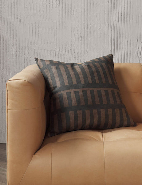 #size::20--x-20- | Kellan square throw pillow sits on a light brown leather sofa in a studio room with textured walls