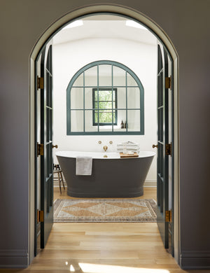The Kate desert palette geometric floor rug sits in a bathroom in front of a black bathtub behind a black-framed arched entrance.
