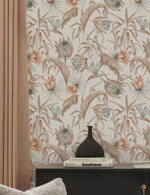 Natural-toned Tropical Wallpaper by Rylee + Cru is in a room with light brown curtains and a black side table with a black vase atop it