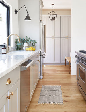 The Masha gray and black geometric machine washable mats lays in a kitchen with stainless steal appliances and marble countertops