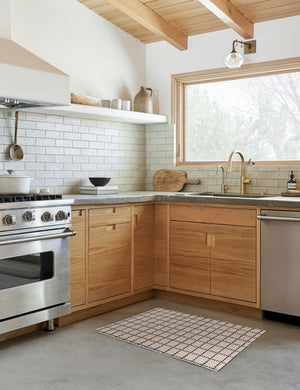 The Sebou natural and black dotted machine washable mat lays in a kitchen with a subway tile backsplash and wooden cabinetry