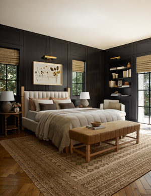  The Ambleside natural linen bed sits atop a patterned rug in a room with accented black wooden walls and a orange linen bench