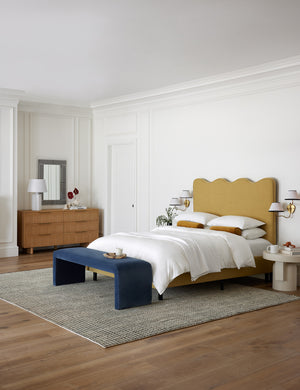 The Uma black and natural checkered grid pattern rug lays under a sculptural golden linen framed bed and a dark navy velvet bench