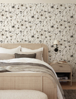 The Scalamandre Lo soft and pastoral brown toned floral wallpaper is in a bedroom with a cane and woven framed bed, gray toned bedding, and a whitewashed wooden nightstand