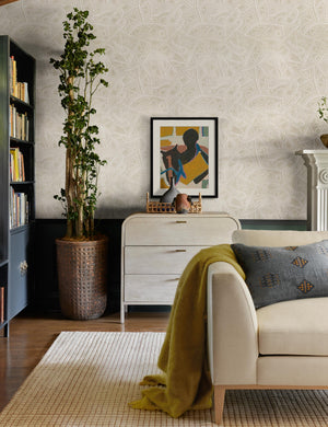 The Uma taupe and natural checkered grid pattern rug lays in a living room with a natural linen sofa and patterned walls