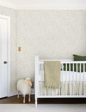 The sommerville natural wallpaper is in a children's room with a sheep toy and a white crib with ivory and blue linens
