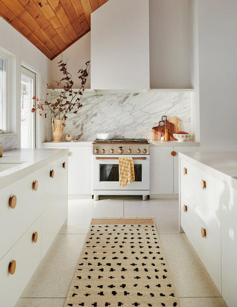 #size::2-6--x-8- | The irregular dots rug in its runner sizes lays in a kitchen with white cabinetry, a brass stove, and sloped wooden-paneled ceilings