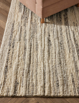 The Rizzoli gray rug sits on a chevron wooden floor under a natural accent chair