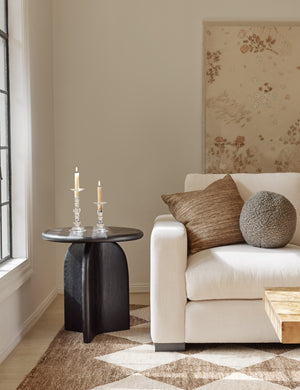  Khaki gray Bouclé Ball Pillow by Sarah Sherman Samuel sits on an ivory couch next to a black side table and atop a patterned rug