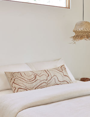 Canyon Terracotta Long Lumbar Pillow lays on a bed with white linens next to a jute pendant light