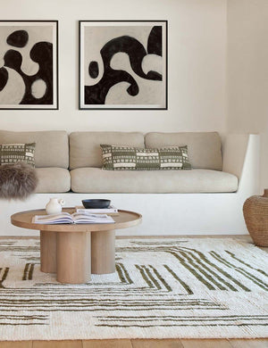 The Stonewalk green geometric throw pillow by Élan Byrd sits on a natural linen cushioned bench next to a round coffee table