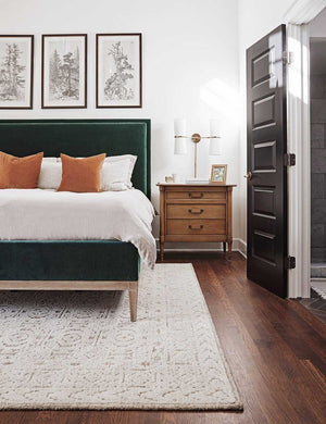 Two Charlotte burnt orange square pillows sit on an emerald velvet framed bed atop a white and neutral textured rug