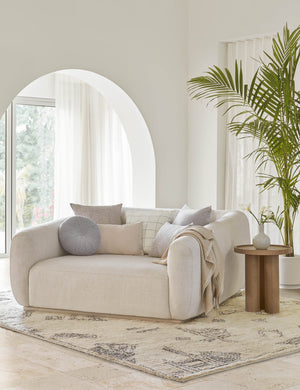 The Monroe ice blue velvet round pillow sits on a white accent chair