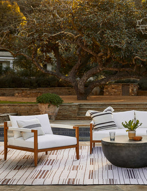 The Fez black and white indoor and outdoor throw pillow sits on a white sofa in an outdoor space atop a rug