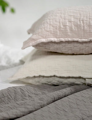 The Ojai greige and light pink Cotton Matelassé Shams with a diamond woven pattern by Pom Pom at Home lay stacked atop each other