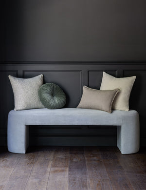 The Monroe moss green velvet round pillow sits on a light blue velvet bench with other throw pillows in a room with black walls