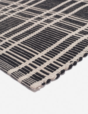 Corner shot of the Rika black and white cotton machine washable mat with checkerboard pattern