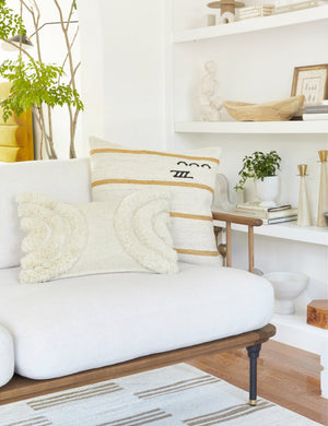 The arches ivory lumbar pillow sits with another decorative throw pillow atop a white linen sofa with a wooden frame
