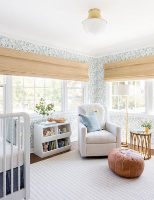  The Randi curved brass Flush Mount Light with domed glass cover is mounted in a nursery with floral wallpaper, white furniture, and a leather ottoman